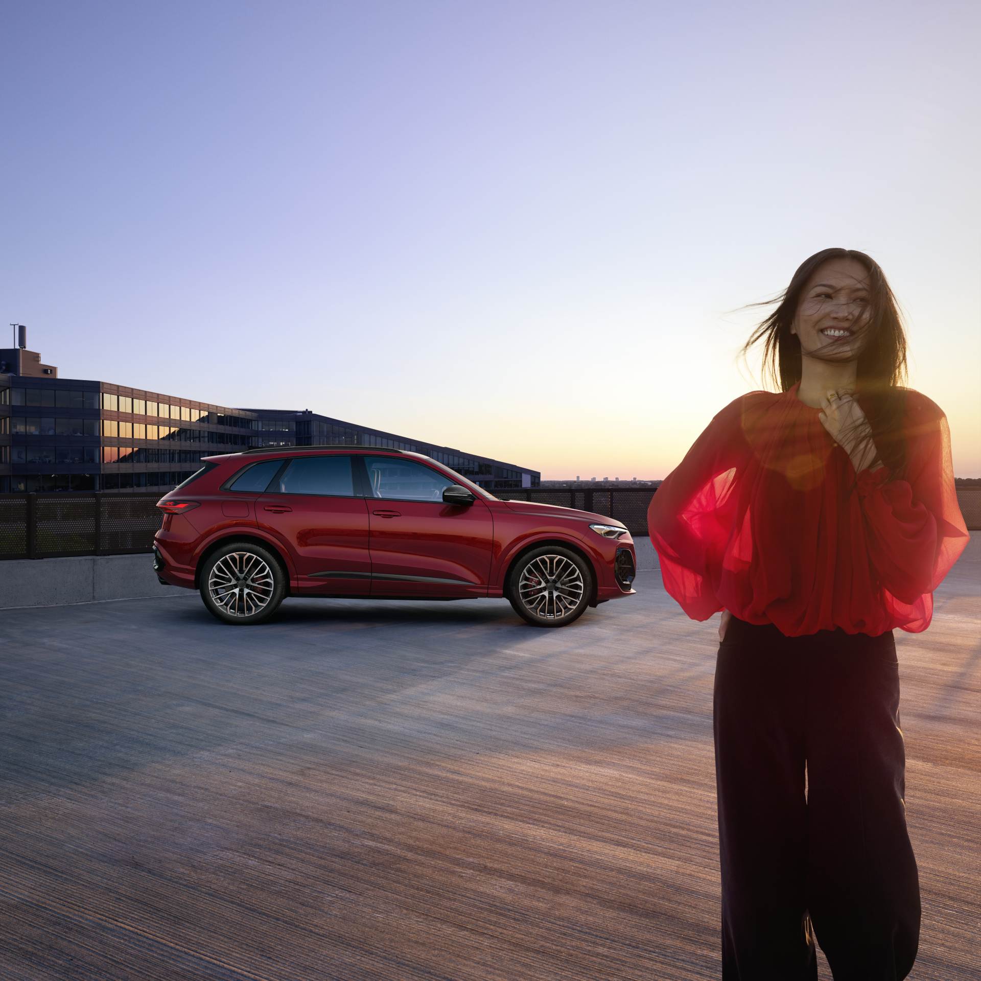 Side profile of an Audi SQ5 parked. A woman is in front of the car, smiling.